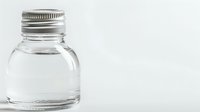 Clear glass bottle with metallic screw cap containing transparent liquid on white background, minimalist composition showing reflection and clean design.