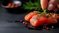 Fresh raw salmon fillet seasoned with herbs, peppercorns and rosemary on dark slate background. Culinary preparation of healthy omega-3 rich seafood.
