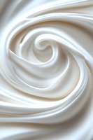 Smooth swirling white cream texture forming spiral pattern, soft silky cosmetic or food background with gentle curves and flowing movement. Macro photography.