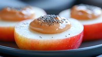 Fresh red apple slices topped with smooth caramel sauce and black poppy seeds on dark plate, macro food photography with selective focus.