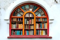 Arched window bookshelf with colorful books behind stained glass, framed by wooden mullions against white wall.