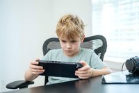 Young blonde boy playing mobile games on tablet device at home desk with concentrated expression for entertainment and technology concept.