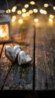 Two silver metal hearts on rustic wooden surface with warm bokeh lights and lantern creating romantic atmosphere for Valentine's Day celebrations.