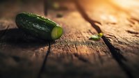 Fresh green cucumber on rustic wooden surface in dramatic lighting, macro food photography with shallow depth of field and dark moody atmosphere.