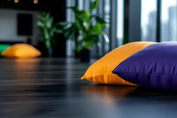 Colorful throw pillows on dark wooden floor with blurred indoor plants in background create cozy modern home atmosphere. Soft focus interior design detail.