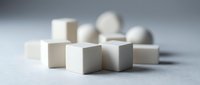 Minimalist white and beige geometric shapes including cubes, cylinders and spheres arranged on neutral surface for modern design projects.