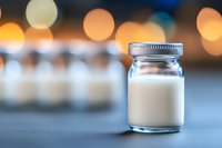 Small glass jar filled with white liquid against blurred warm bokeh background, minimalist composition highlighting freshness and purity of dairy product.