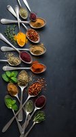Colorful spices and herbs in vintage metal spoons arranged on dark slate background. Culinary ingredients for cooking and seasoning food preparation.