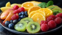 Fresh colorful fruit platter with sliced oranges, kiwi, raspberries, blueberries, and peaches arranged on dark plate, macro food photography with soft lighting.