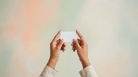 Woman with medium skin tone holding blank white card against soft pastel background, suitable for business messaging, marketing campaigns, and promotional content.