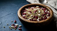 Mixed legumes and beans in rustic wooden bowl on dark slate surface with linen cloth. Healthy protein-rich ingredients for cooking and meal preparation.
