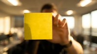 Young adult male with medium skin tone holding translucent yellow square panel in modern office setting with blurred background, representing innovation and transparency.