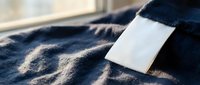 Young woman relaxing on soft blanket with blank white card or note, cozy indoor lifestyle moment with warm natural lighting and textile textures.