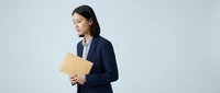 Young Asian woman in dark navy blazer holding yellow folder, standing against white background, suitable for corporate, business, and professional website design.