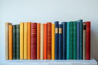 Row of vintage hardcover books in various colors including yellow, green, orange, red and blue standing on white wooden shelf against light gray wall background.