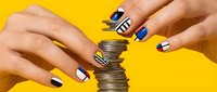 Woman with manicured nails featuring geometric patterns in blue, white, and black designs stacking coins against bright yellow background for finance and savings concepts.
