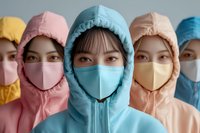 Young Asian women wearing protective face masks and colorful hooded protective suits standing in row, focus on person in blue center position.