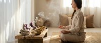 Young Asian woman practicing meditation in serene home setting with burning incense, crystals and wooden altar creating peaceful mindfulness atmosphere.