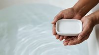 Bar of soap in hands of person with dark skin tone over water surface, suitable for hygiene, wellness, and personal care product marketing.