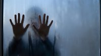 Silhouette of hands pressed against frosted glass window with condensation droplets creating mysterious atmospheric mood for horror thriller concepts.
