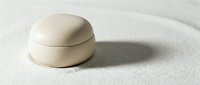 Minimalist cream jar resting on raked white sand, evoking zen spa aesthetics for skincare, wellness, and beauty product advertising.