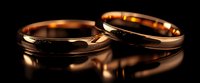 Golden wedding rings on dark reflective surface with warm lighting and dramatic shadows create romantic atmosphere for marriage and commitment symbolism.
