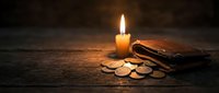 Burning candle illuminating leather wallet with scattered coins on rustic wooden surface creating warm atmospheric lighting for financial concepts.