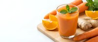 Fresh carrot orange ginger juice in glass on wooden board with mint, citrus slices and raw carrots on white background.