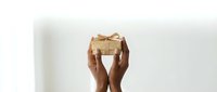 Hands holding elegant gift box with golden ribbon bow against clean white background for special occasions and celebrations.