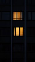 Illuminated windows with warm yellow curtains glowing in dark apartment building facade create mysterious atmospheric night urban scene.