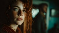 Young redhead woman with curly hair in dramatic lighting, contemplative expression, cinematic portrait with bokeh background for storytelling projects.
