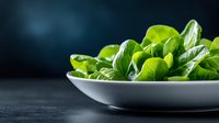 Fresh green spinach leaves served in white ceramic plate on dark background with copy space, healthy eating and nutrition concept.