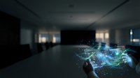 Young male professional, Caucasian appearance, wearing business attire, holding digital holographic network interface with glowing blue and green data visualization in modern office space.