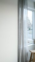 Gray linen curtains hang beside a bright window in a minimalist interior space, allowing natural light to filter through the fabric for home decor and window treatment design.