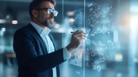 Middle-aged Caucasian businessman in suit writing financial formulas and data analytics on transparent glass wall in modern corporate office environment.
