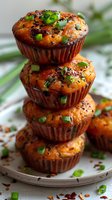 Savory muffins stacked in tower, garnished with green onions and spices on white plate, blurred green background.