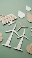 Handcrafted paper cutout icons of wind turbines, solar panels, leaves, and water drops on green background, symbolizing renewable energy and sustainability.