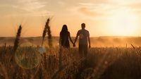 Romantic couple silhouettes holding hands walking through golden wheat field at sunset with warm orange sky and peaceful countryside atmosphere.