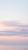 Serene ocean horizon with soft pink and purple sunset clouds reflecting on calm water surface creating peaceful seascape atmosphere.