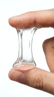 Clear gel or slime stretching between two fingers demonstrating elasticity and viscosity. Suitable for skincare, cosmetics, beauty product marketing, and scientific or educational content about polymers and textures.