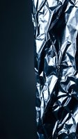 Crumpled metallic silver foil with dramatic lighting creates abstract textural patterns against dark background for modern design projects.