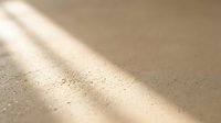 Warm sunlight casting soft shadows across fine golden sand texture with natural grain patterns creating peaceful minimalist background for relaxation concepts.