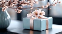 Elegant gift box in soft turquoise with pink ribbon and delicate cherry blossoms on top, creating romantic composition against blurred background for special occasions.