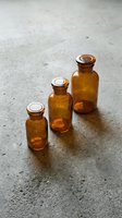 Three amber glass bottles with cork stoppers arranged on concrete surface, suitable for essential oils, aromatherapy, pharmaceuticals, or cosmetic product packaging and branding.