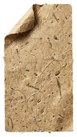 Handmade brown paper sheet with natural plant fibers and organic materials embedded in textured surface isolated on white background for craft projects.