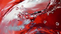 Dynamic splash of red liquid with transparent water drops creating abstract pattern against white background. Macro photography captures motion and bubbles.
