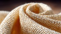 Macro shot of cream colored braided rope texture showing detailed weave pattern and soft curves against blurred background for design and textile concepts.