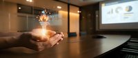 Business professional holding glowing lightbulb with innovation icons in modern conference room during presentation meeting.