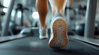 Close-up view of athletic shoes on treadmill showing sole pattern while running, focused on feet movement in modern fitness gym with blurred background.