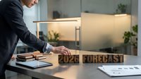 Professional businessman analyzing 2026 forecast with wooden letter blocks on modern office desk during strategic planning session.